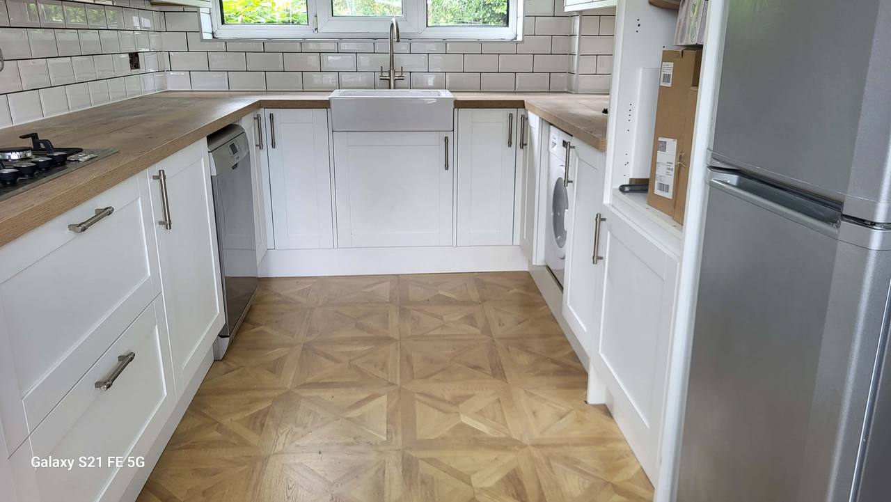 Renovated kitchen with white shaker units, oak-effect worktops, a ceramic Belfast sink under the window, metro-tiled walls and parquet-pattern flooring