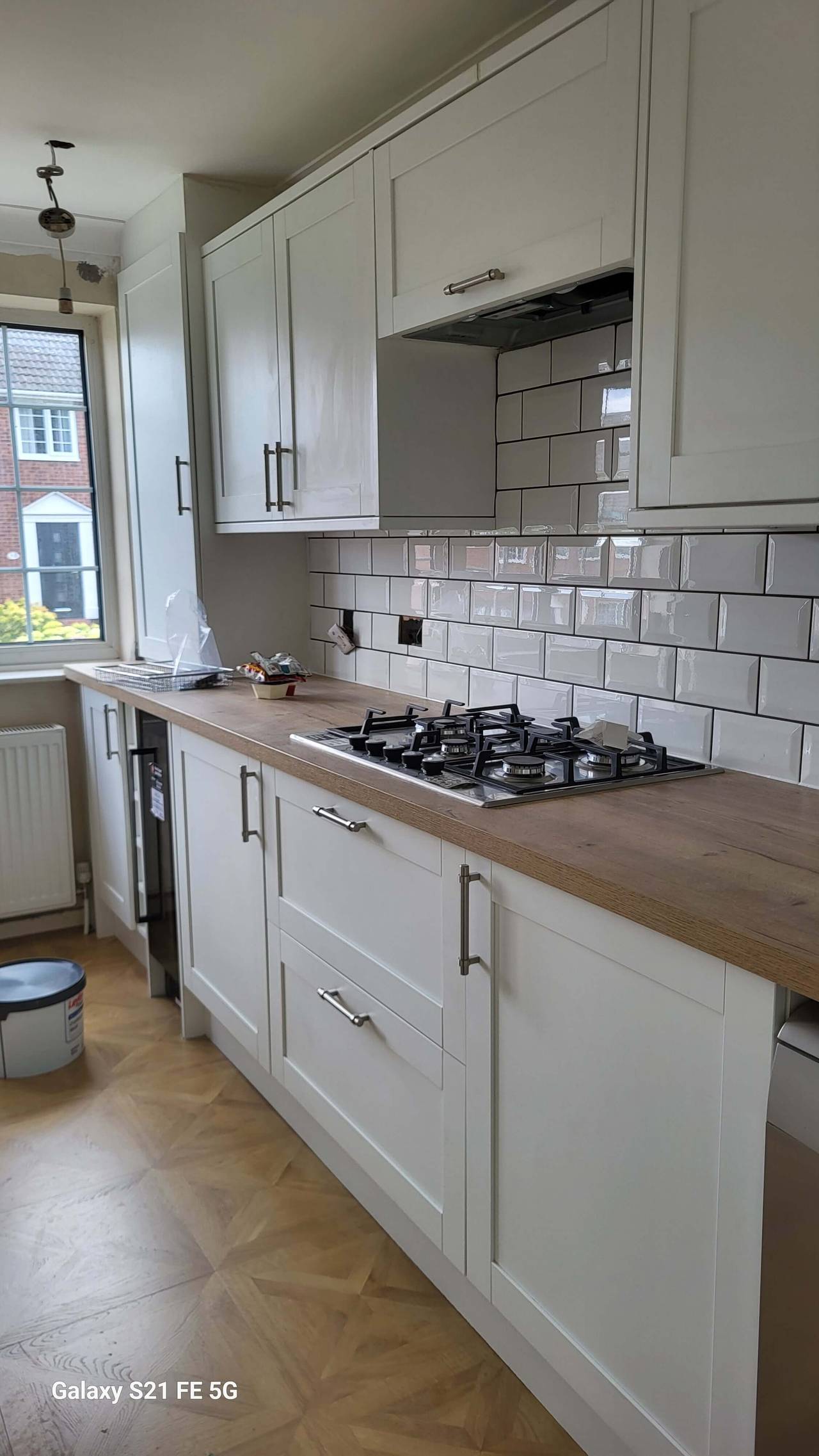 New kitchen with white shaker cabinets, a gas hob and stainless extractor, white metro tiles and an oak-effect worktop