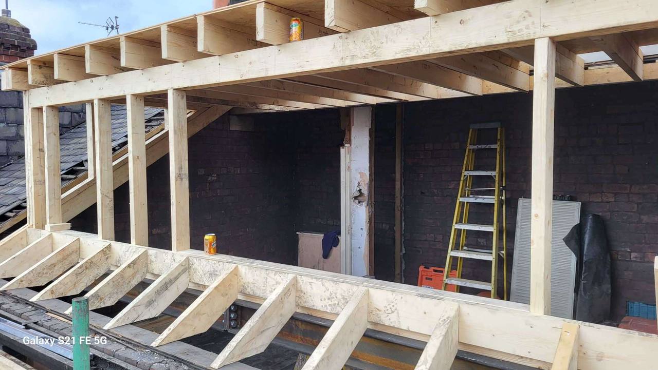 Open timber framework of a full-width rear dormer loft conversion, with new joists and studwork against the brick gable