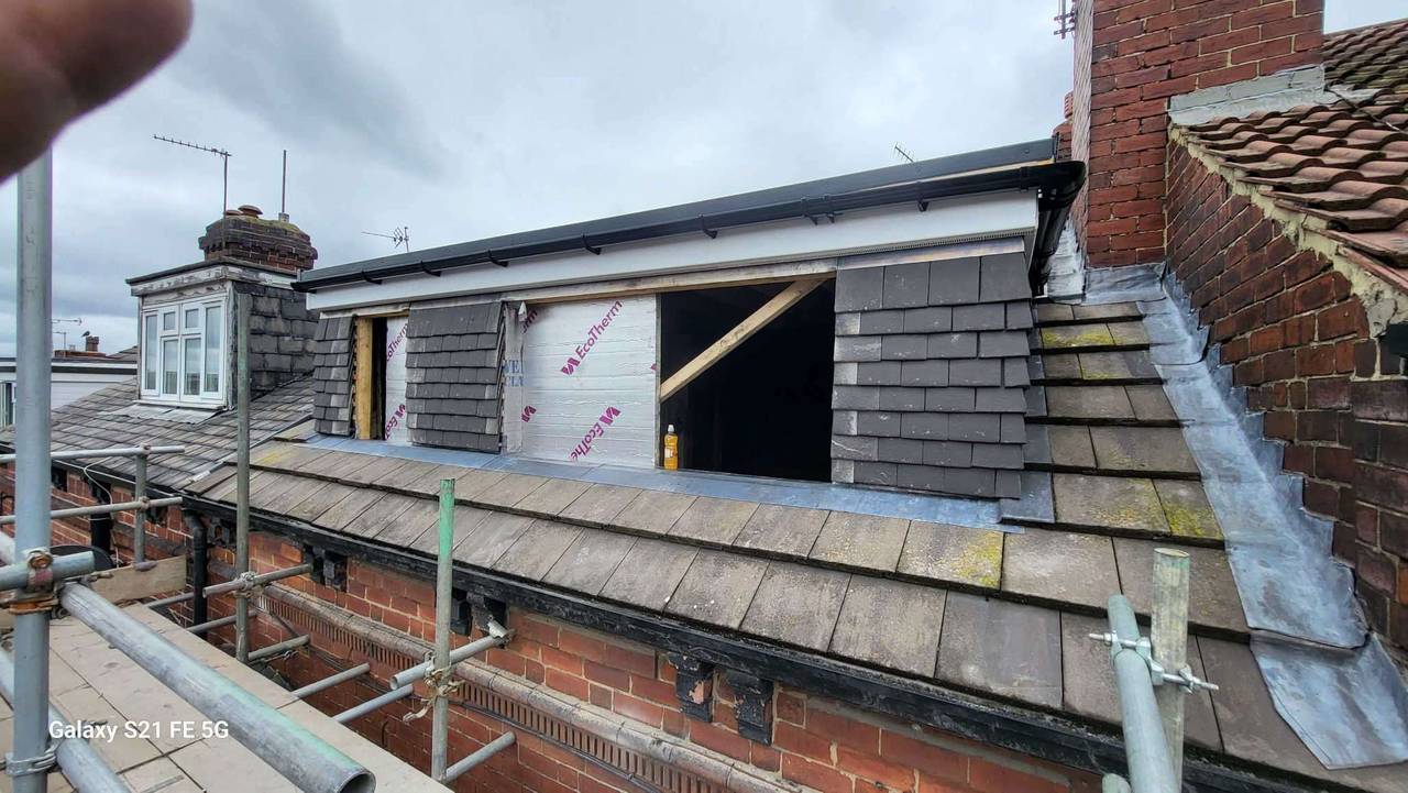 Box dormer loft conversion taking shape on a terraced house roof, clad in grey slate-effect tiles with insulation boards and window openings
