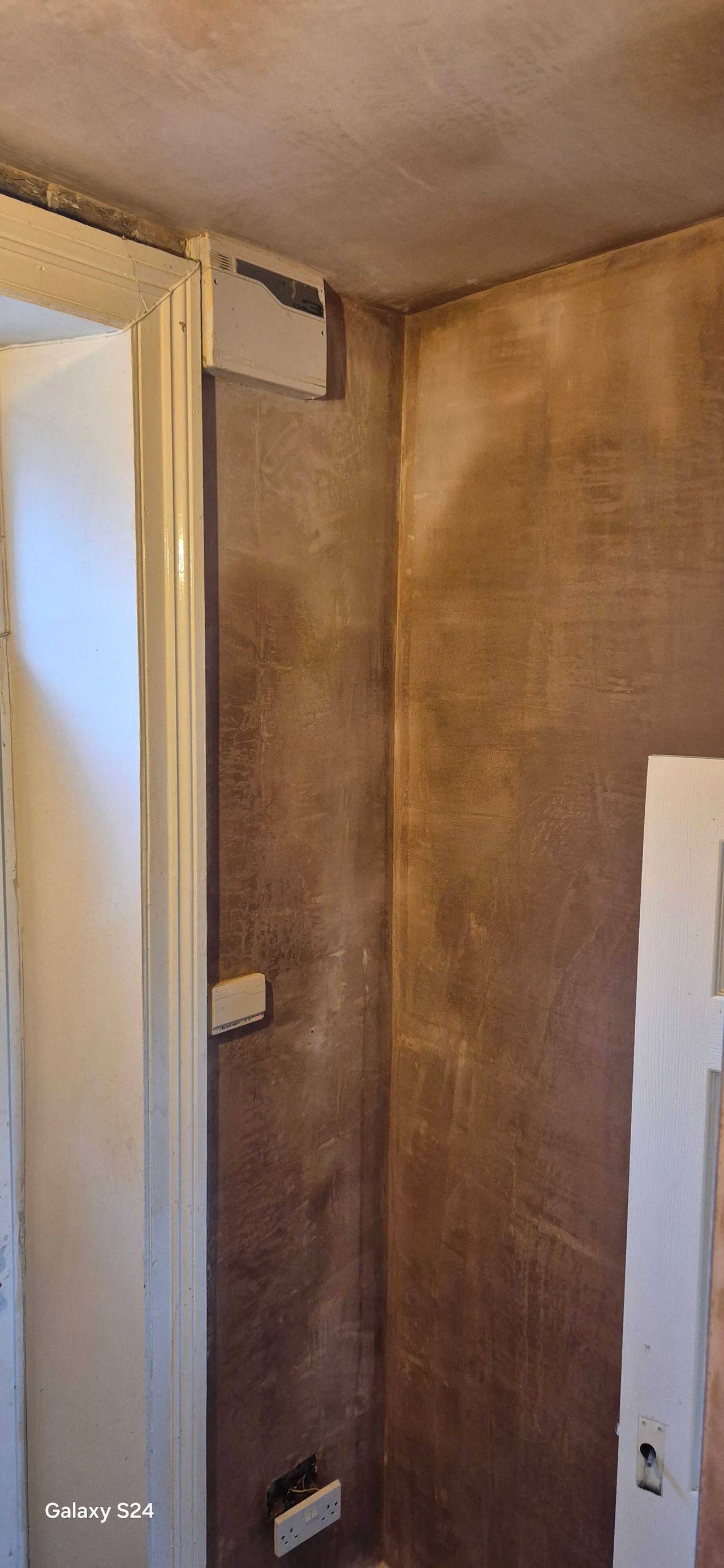 Newly skimmed plaster walls drying in the corner of a room beside a white door frame