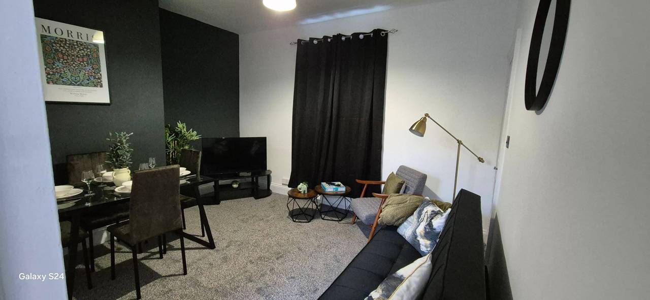 Renovated open-plan living and dining room with a dark green feature wall, grey carpet, a sofa and a brass floor lamp