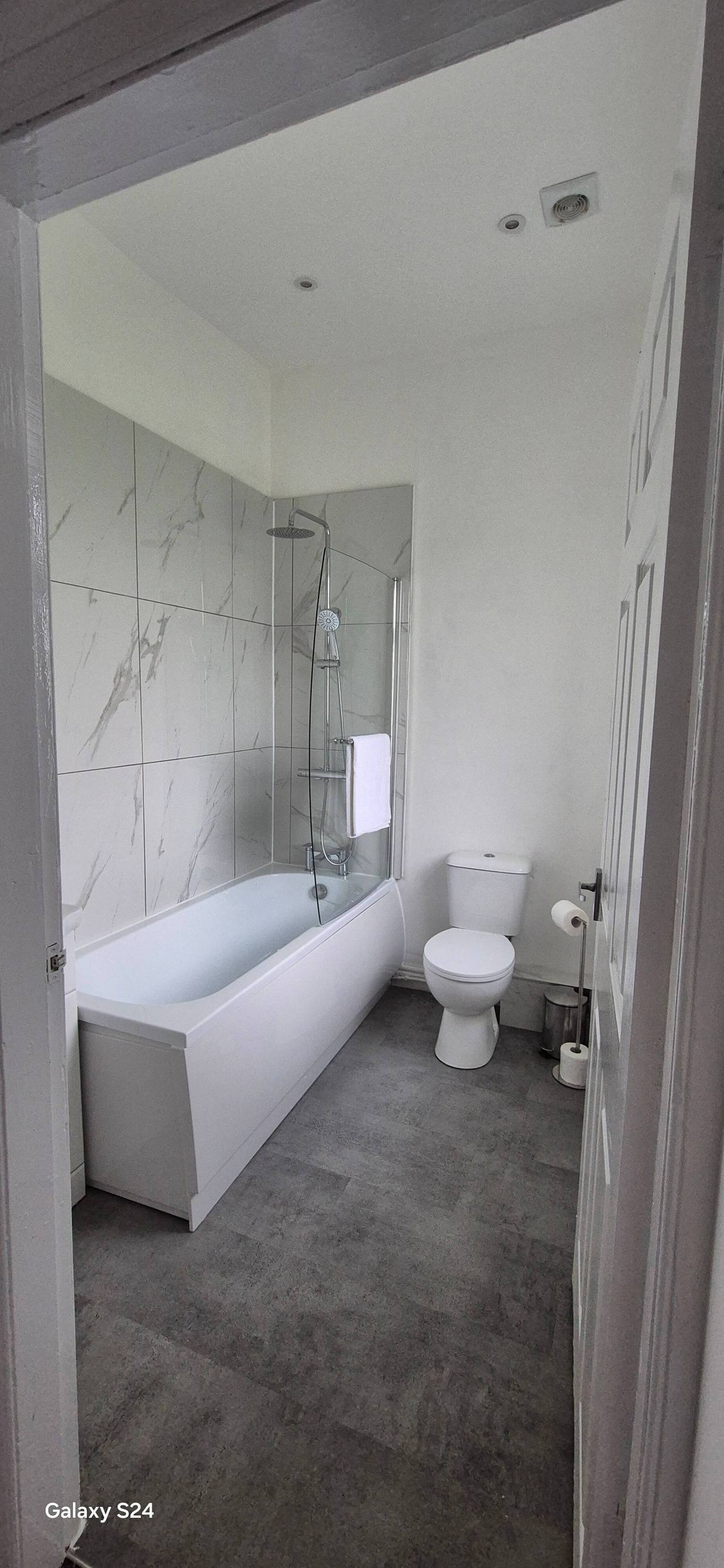 Renovated family bathroom with a white bath and glass shower screen, large marble-effect wall tiles and grey tiled flooring