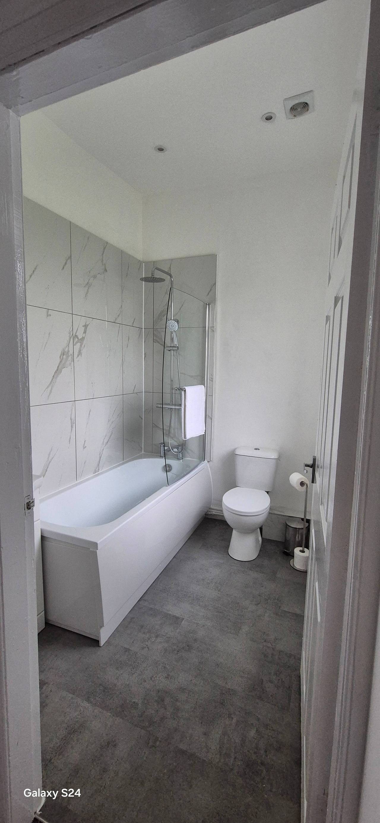 Renovated family bathroom with a white bath and glass shower screen, large marble-effect wall tiles and grey tiled flooring