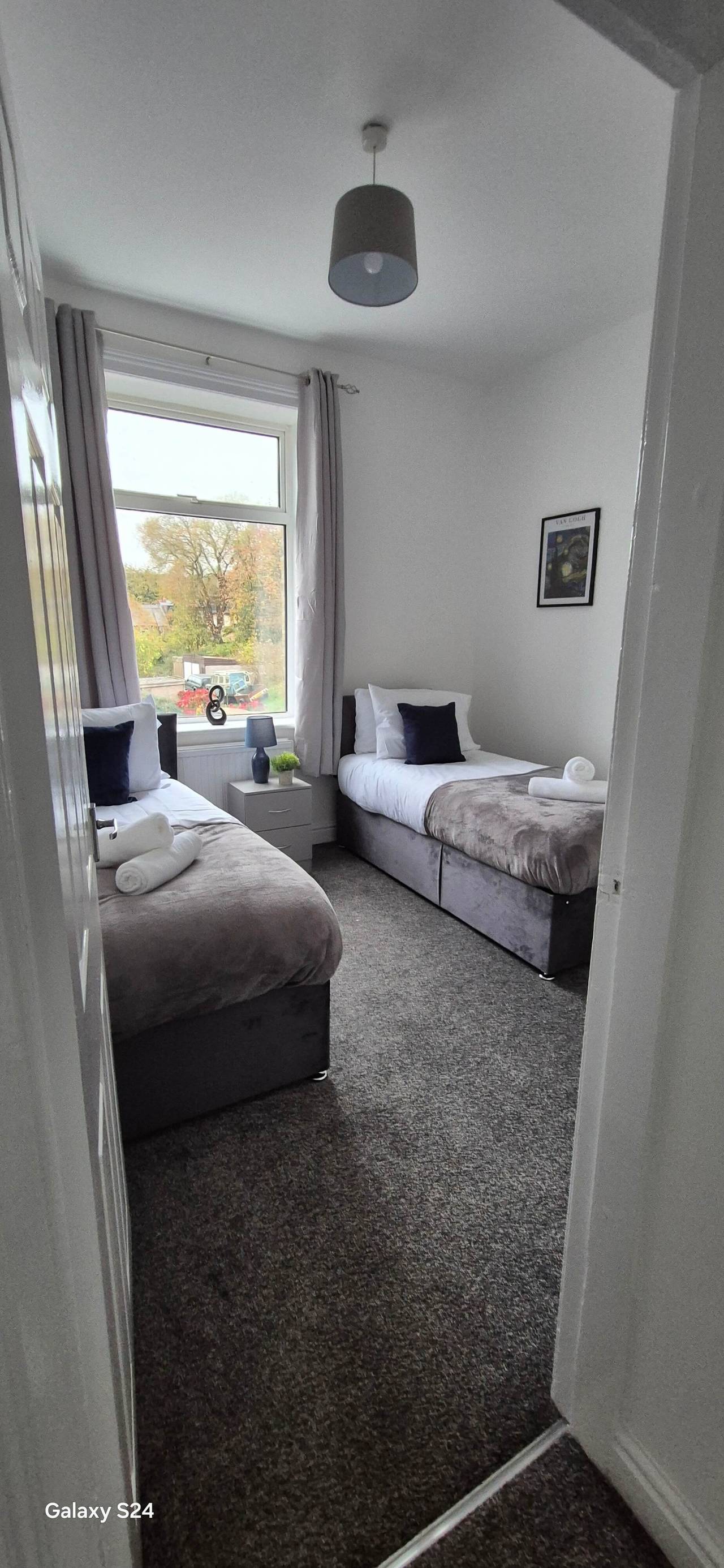 Newly finished twin bedroom with two grey upholstered beds, charcoal carpet and fresh white walls