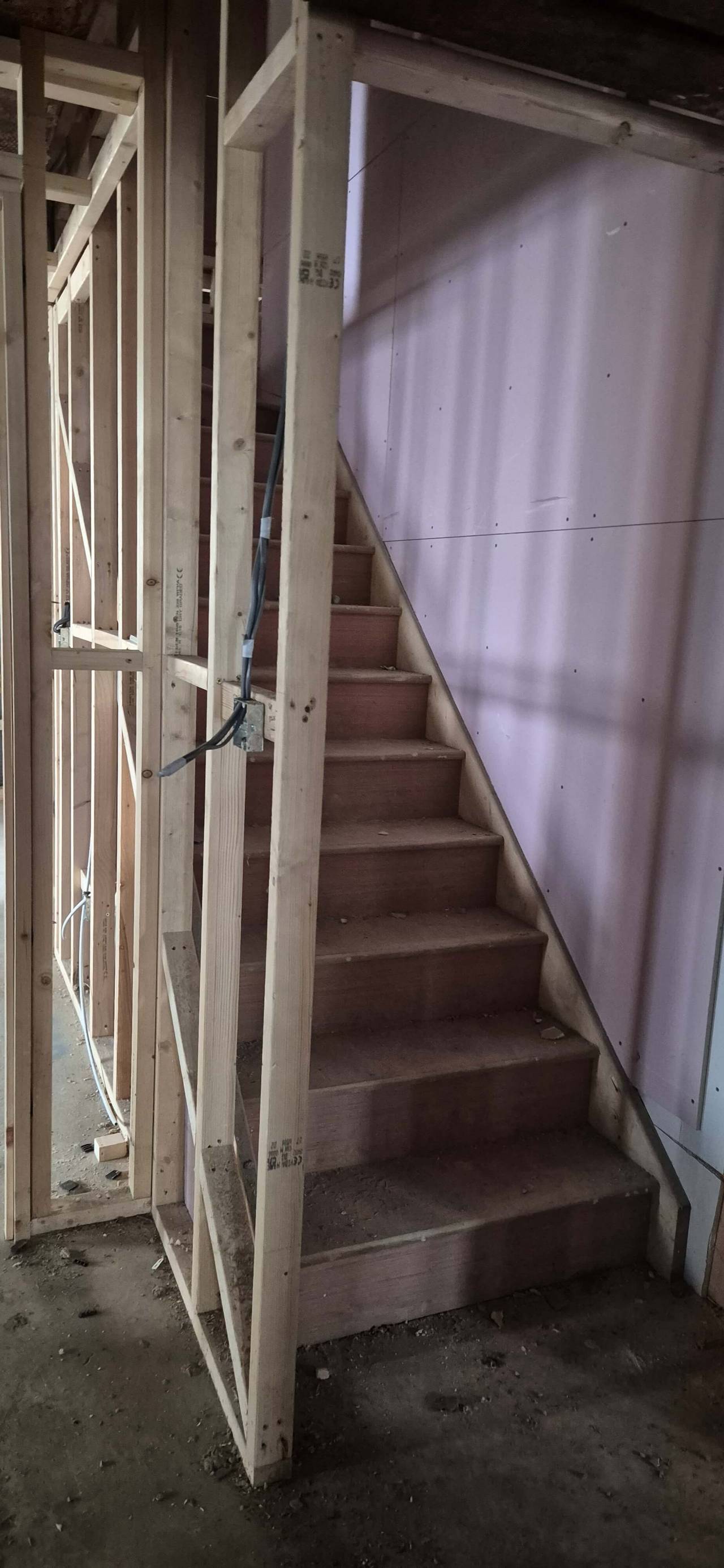 New softwood staircase beside timber stud walls with first-fix electrics, during a renovation