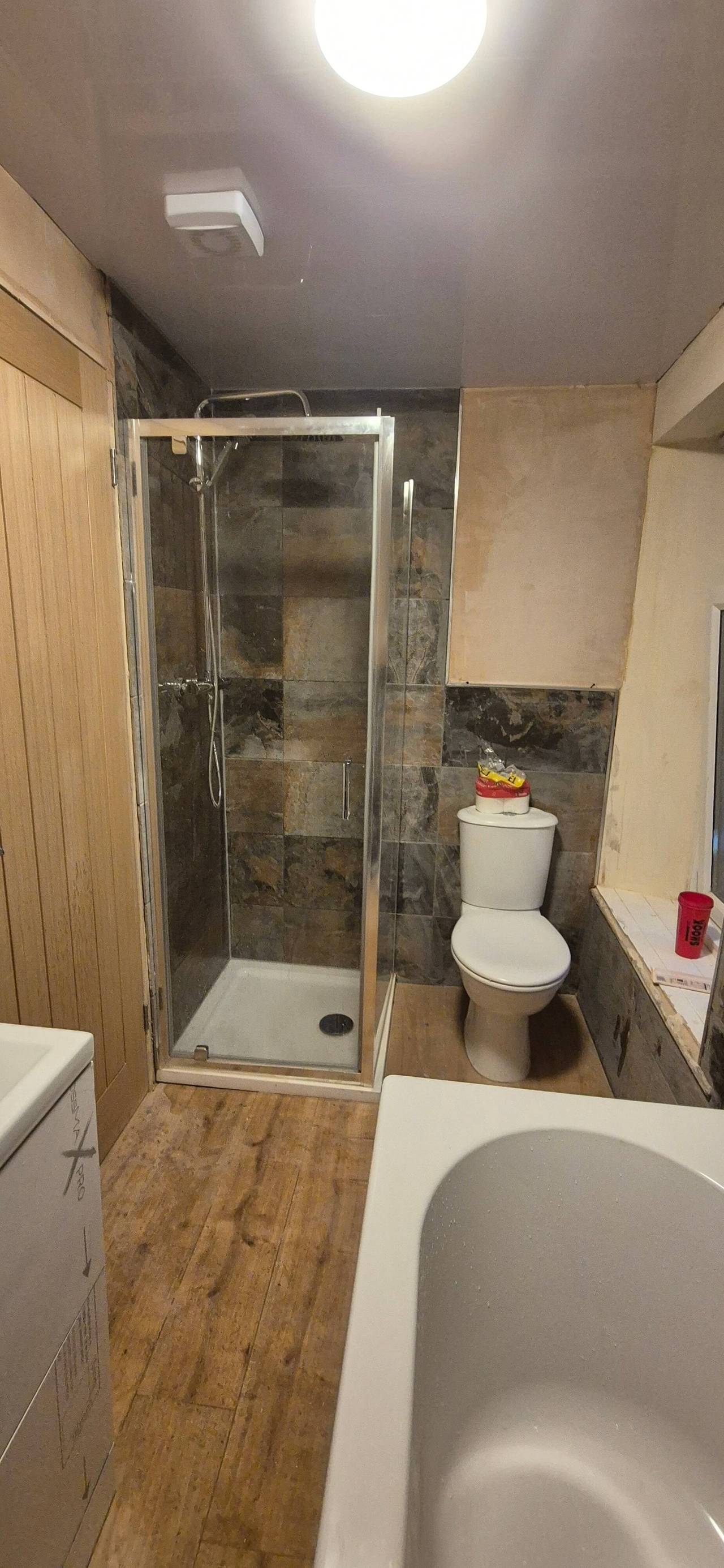 Bathroom refit in progress with a corner shower enclosure, slate-effect wall tiles, a new WC and wood-effect flooring