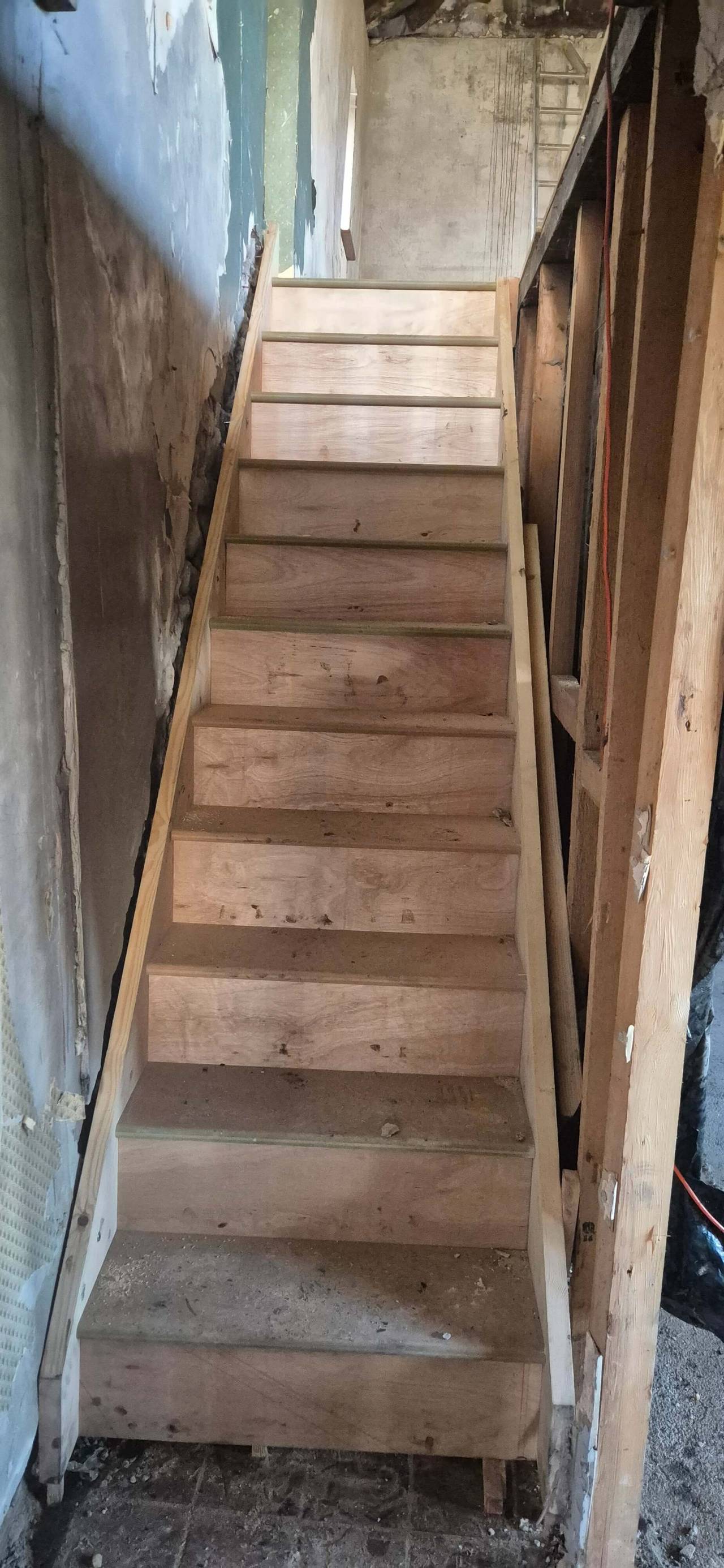 Newly built timber staircase rising between a stud wall and a bare stone wall during a renovation