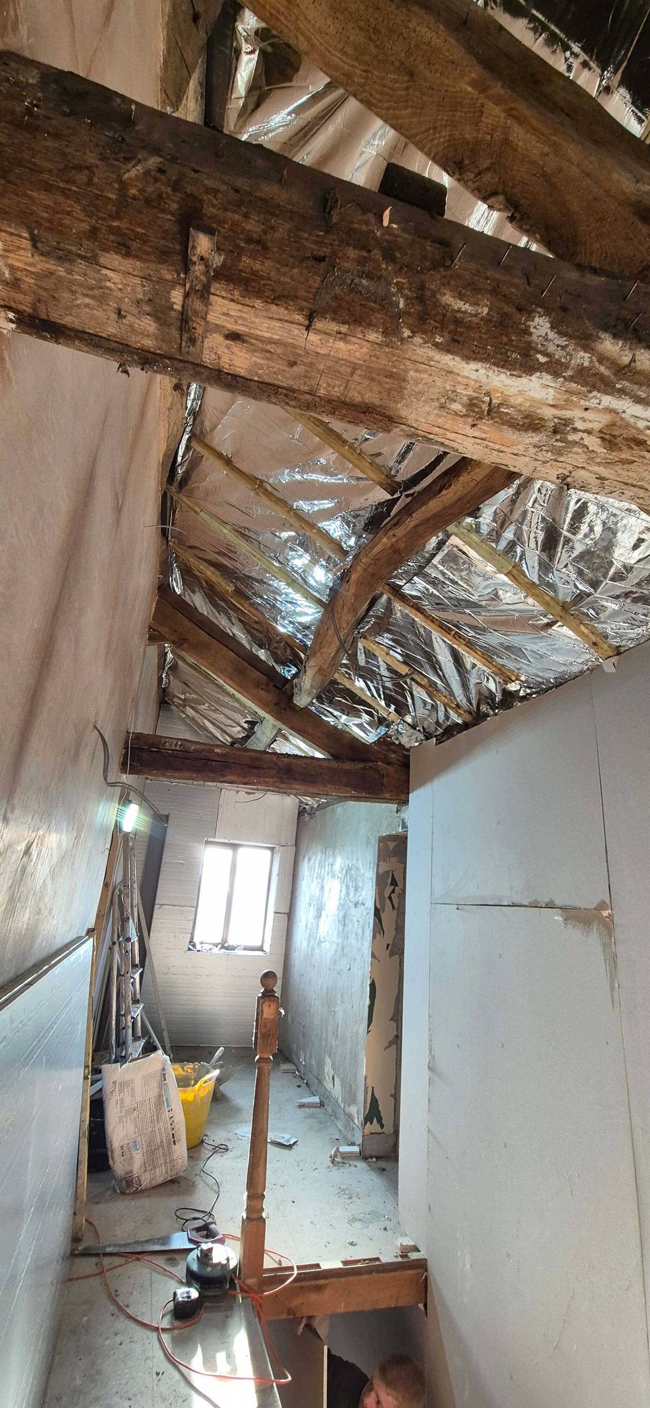 Original timber roof beams exposed above a new attic room, with multifoil insulation between the rafters and fresh plasterboard walls