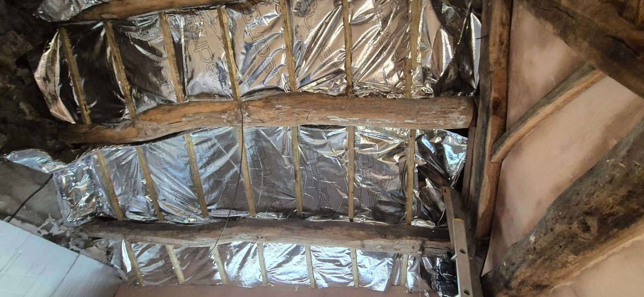 Reflective multifoil insulation fitted between rafters and around old timber purlins in an attic roof