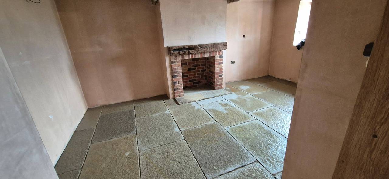 Renovated room with a newly laid stone flag floor, fresh plaster walls and a restored brick fireplace