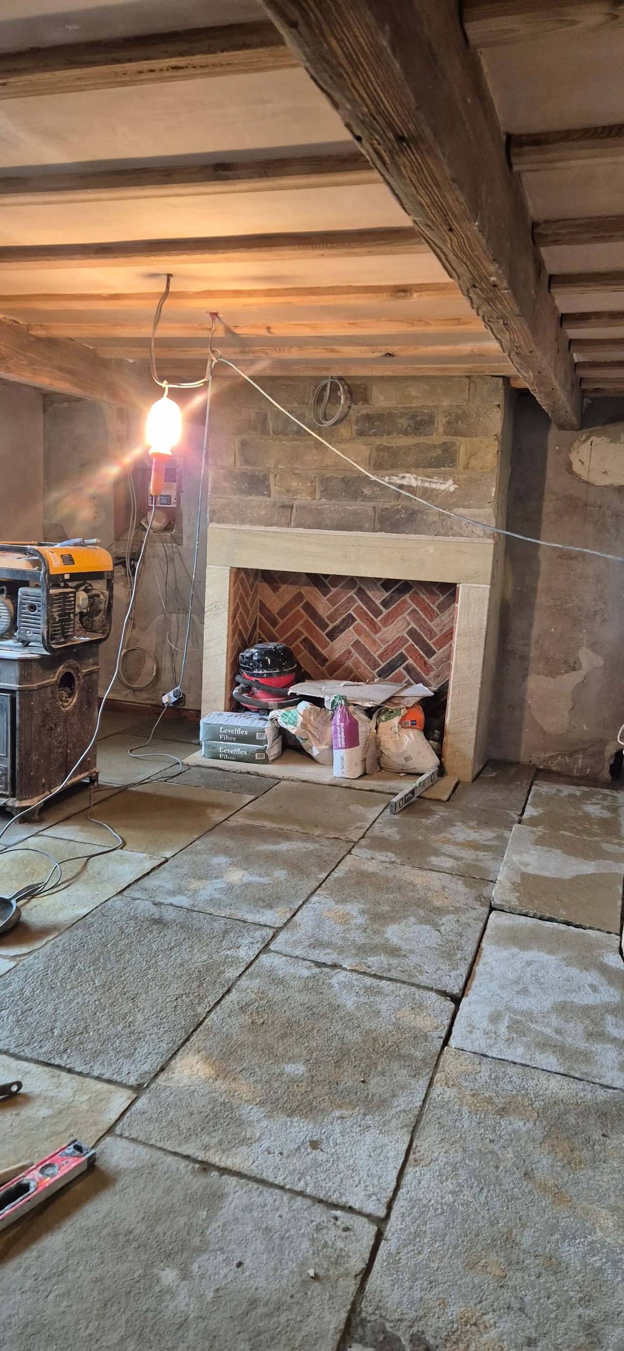 Cottage room mid-renovation with a stone flag floor, exposed ceiling beams and a new stone fireplace surround with a herringbone brick back