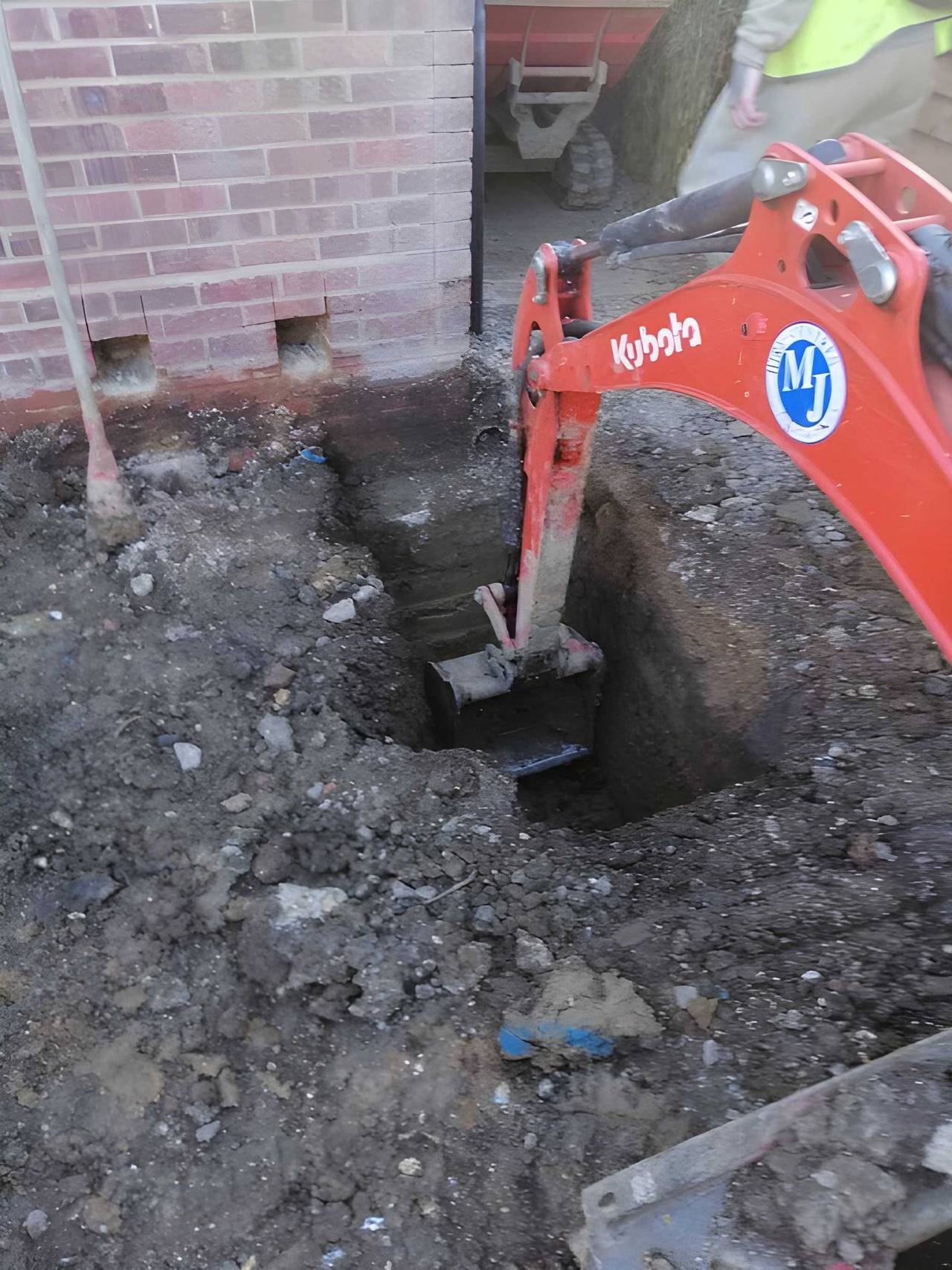 Mini digger excavating a foundation trench beside a brick house