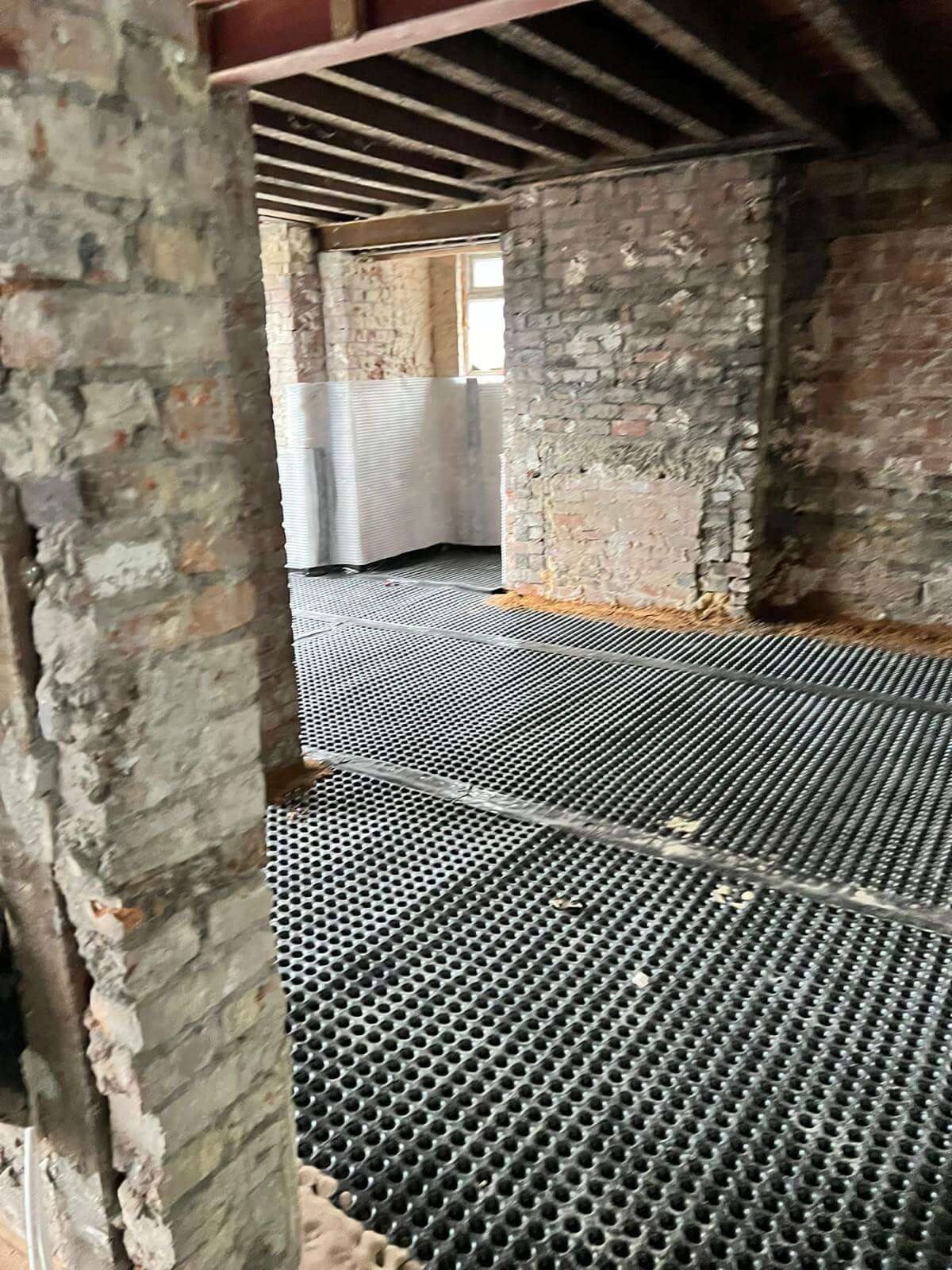 Room stripped back to bare brick with a studded drainage membrane laid across the floor during damp-proofing works