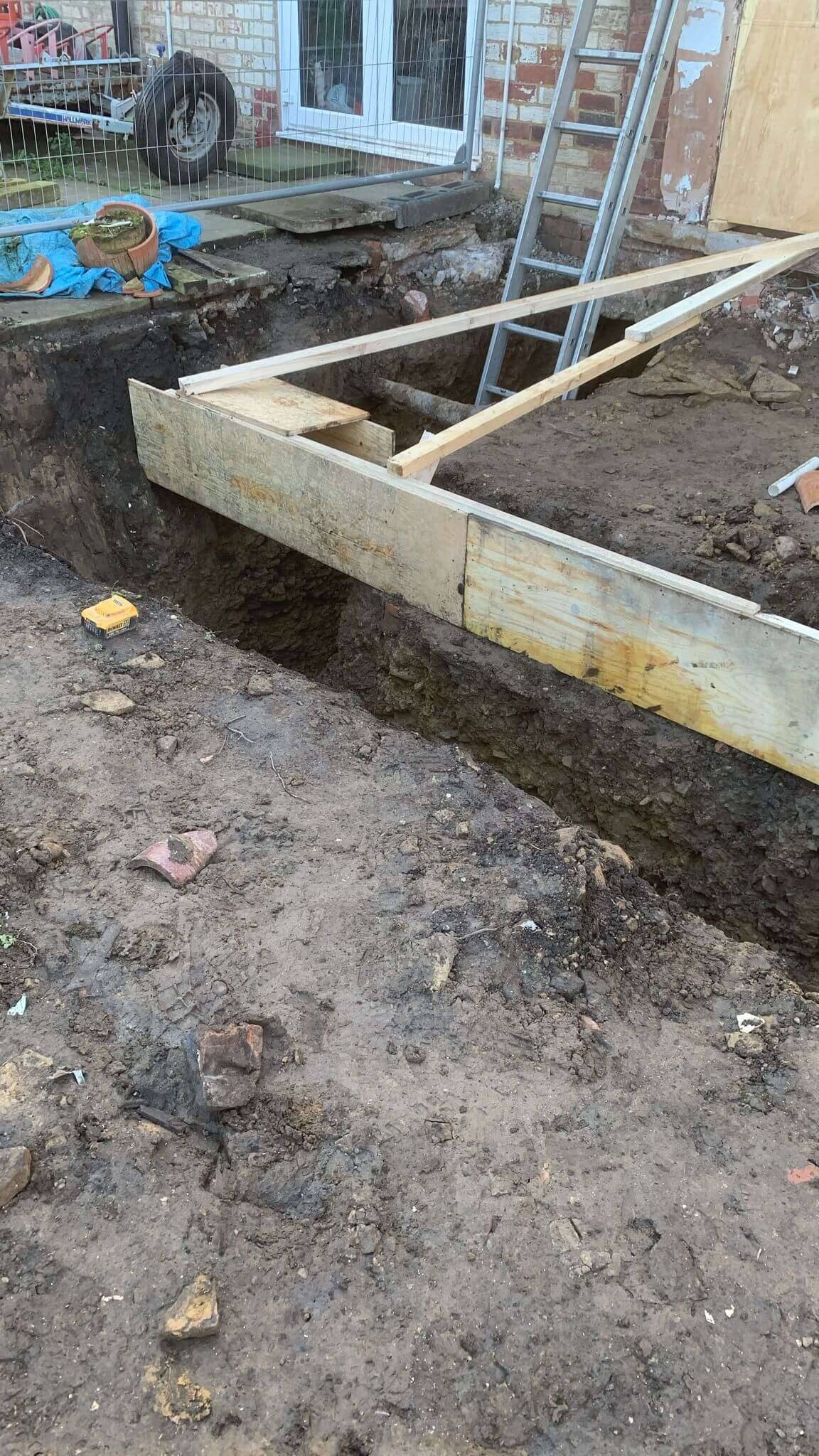 Timber shuttering set along a freshly excavated extension foundation trench at the back of a house