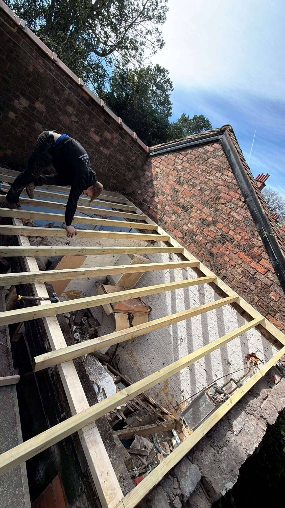 Builder fixing new timber rafters on a lean-to extension roof against a red-brick gable wall