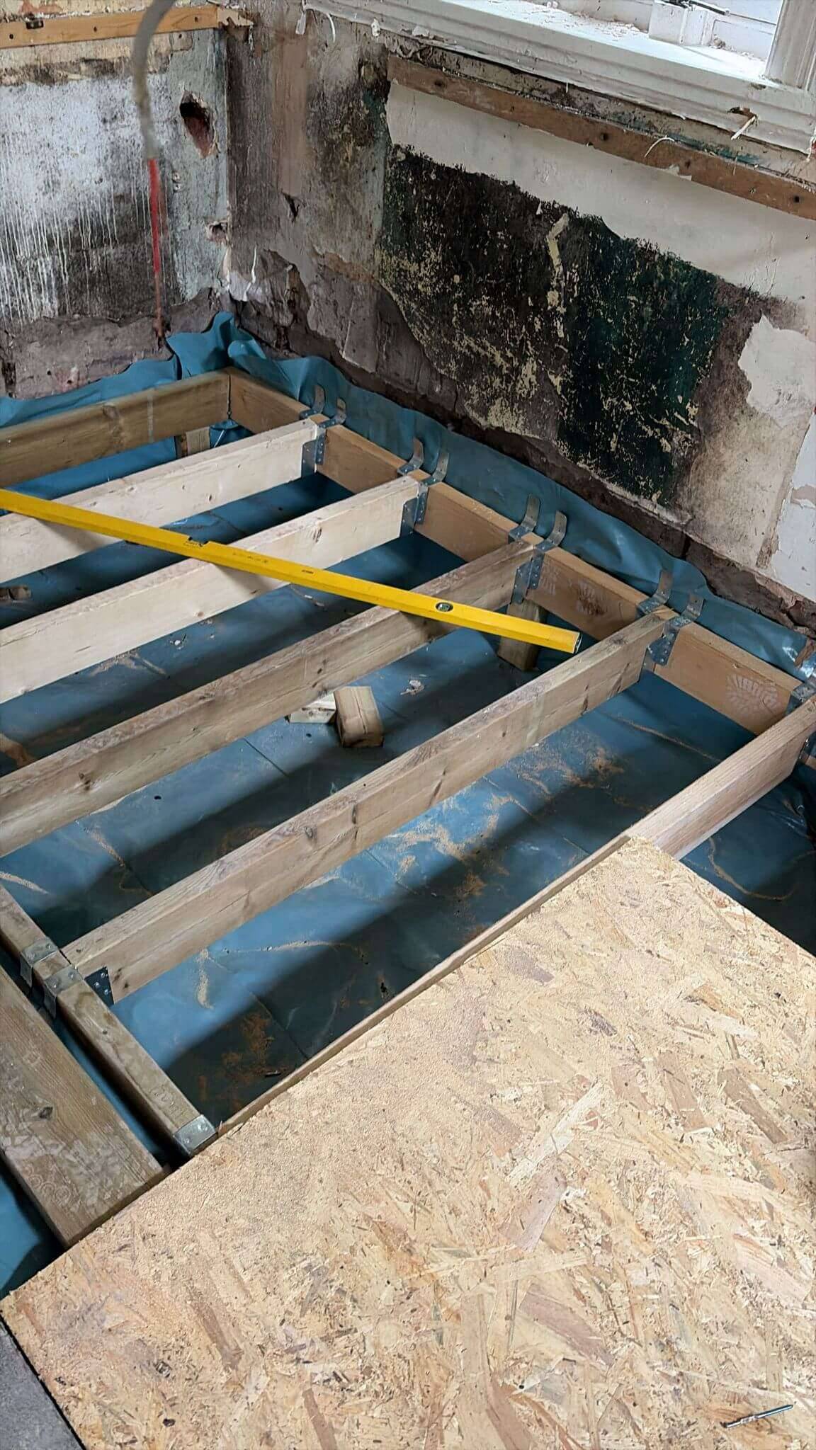 New floor joists on steel hangers over a damp-proof membrane, partly boarded with OSB, in a stripped-back room