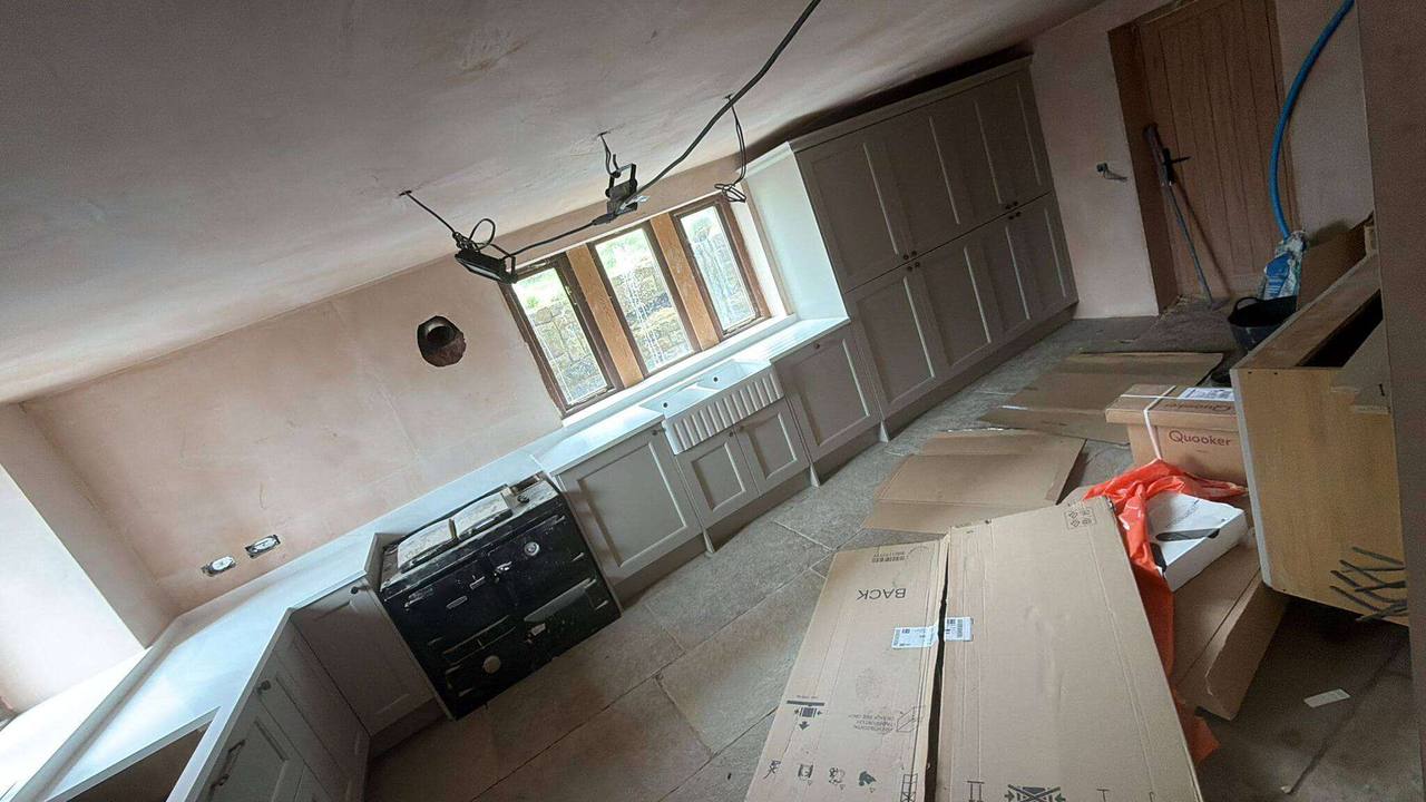 Shaker-style kitchen being fitted in a cottage, with a black range cooker and a Belfast sink beneath leaded windows
