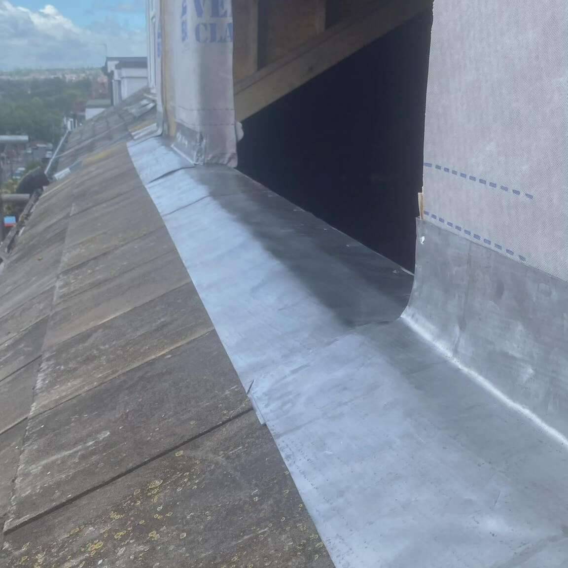 New lead flashing dressed along the base of a dormer on a slate roof, with views across the rooftops