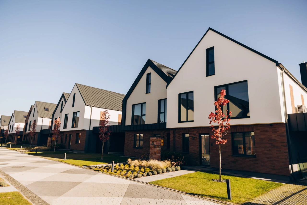 Row of newly built gable-fronted homes in white render and red brick along a sunlit street